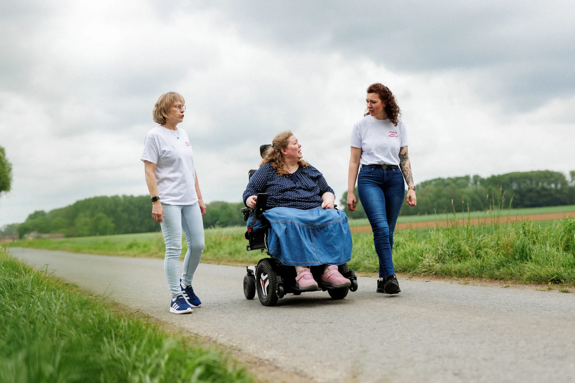 florence-hilfe-daheim-begleiteter-spaziergang-zwei-betreuerinnen Zwei Pflegekräfte von Florence Hilfe und Daheim ambulante Pflegestation begleiten eine Frau im Elektrorollstuhl auf einem Feldweg