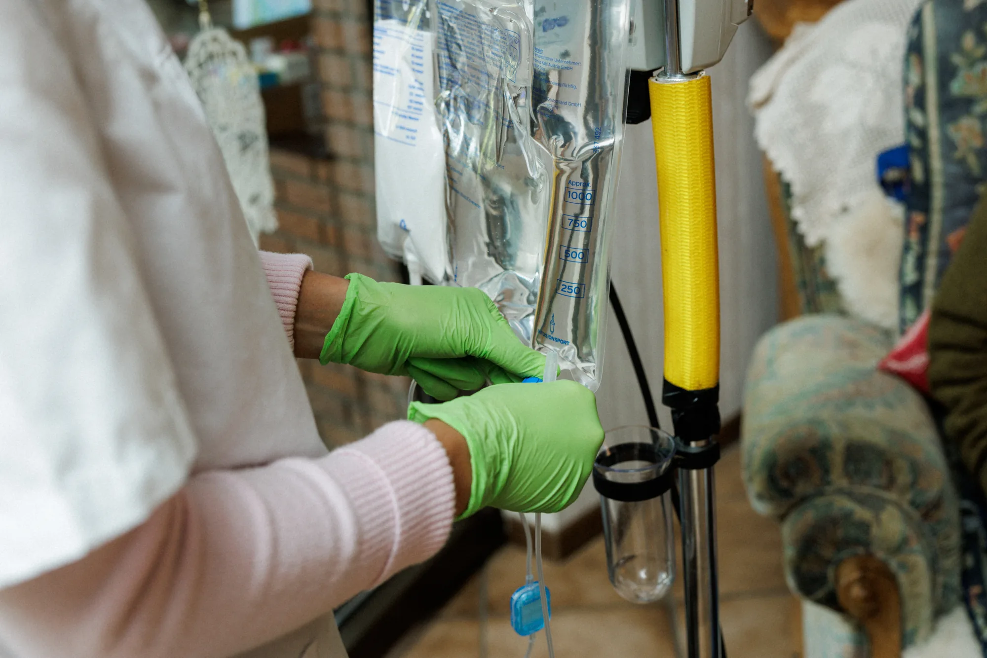 Pflegefachkraft mit Schutzhandschuhen bereitet eine Infusion am Infusionsständer vor