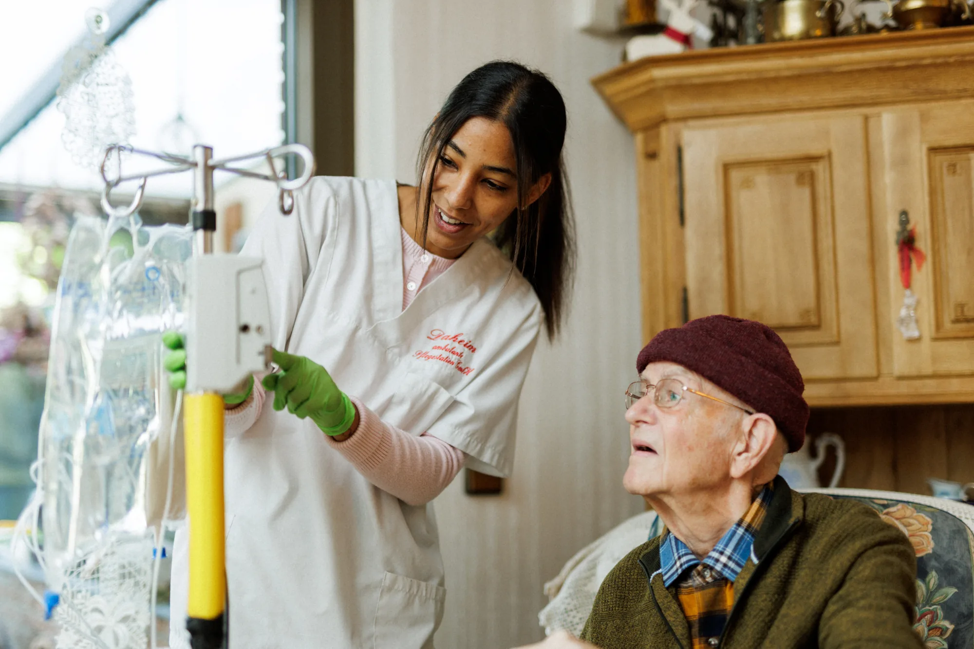 Pflegefachkraft von Florence Hilfe richtet eine Infusion ein, während der Patient zusieht